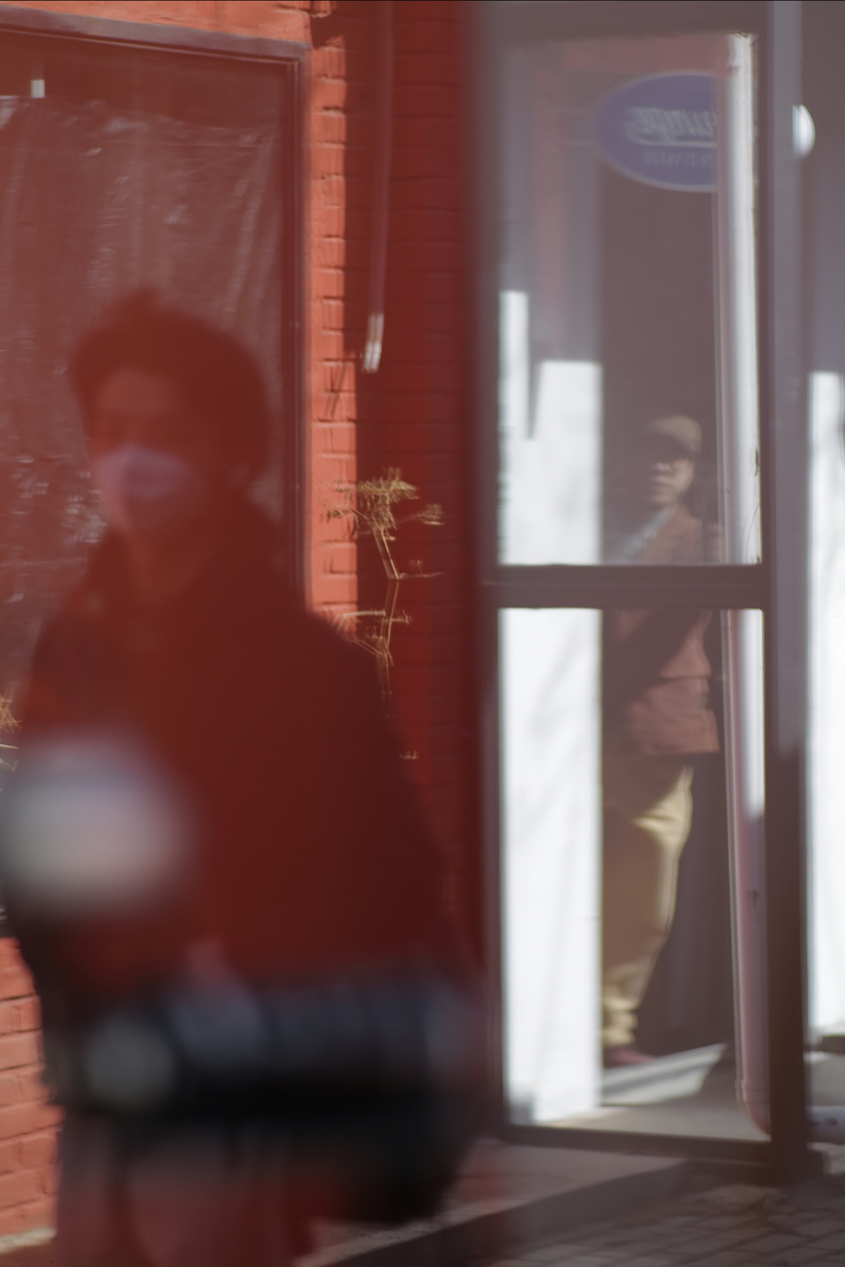 一个人戴着口罩走过一座建筑 窗户里反射出一个男人的身影。