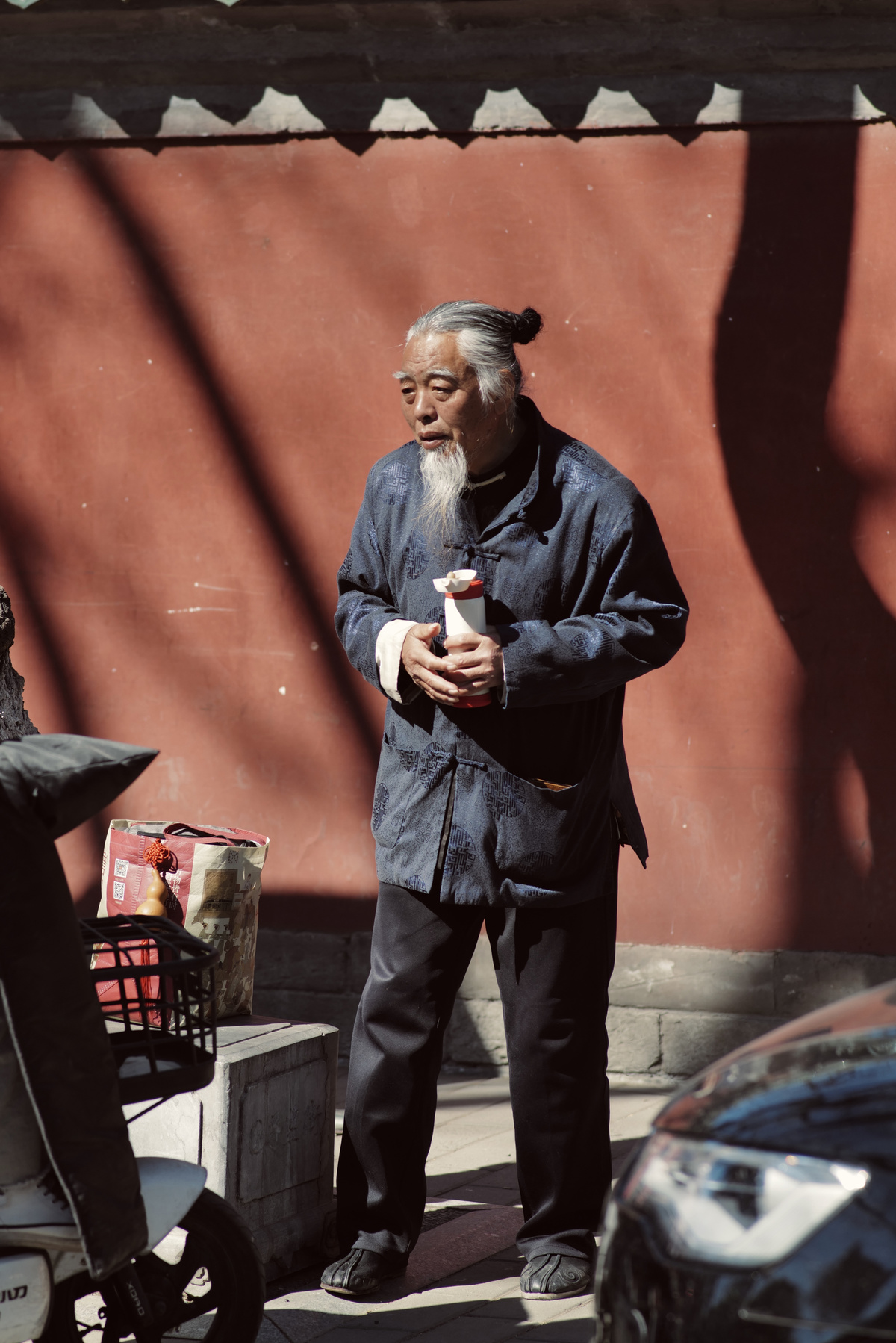 一个留胡子的老人站在人行道上 前方是红色的墙。