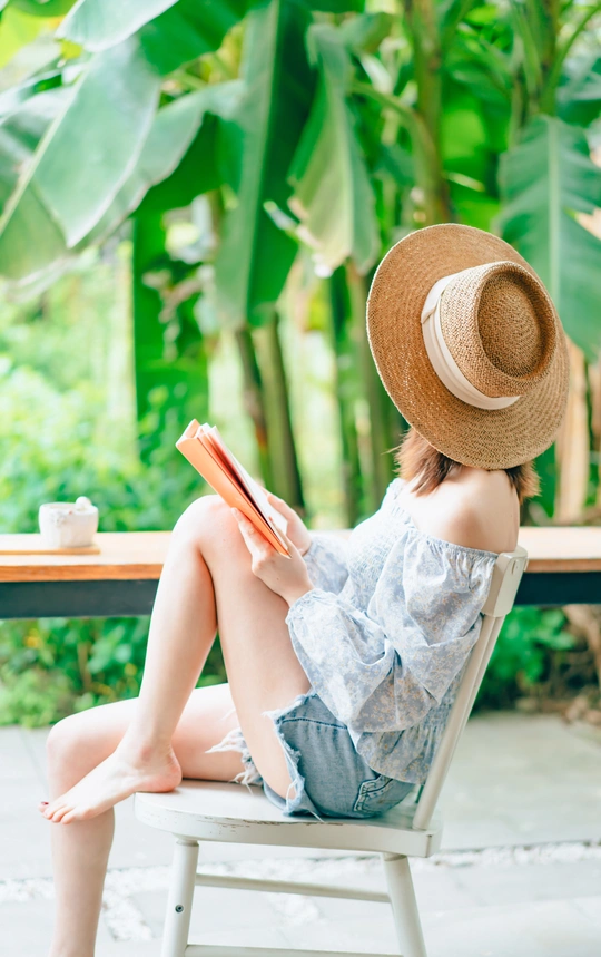 一个戴着帽子的年轻女人坐在外面的椅子上看书