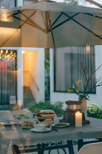 户外餐桌 伞下放着一花瓶鲜花、蜡烛和几盘食物