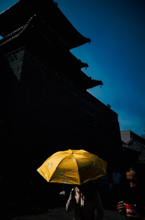 一位站在建筑物前夜间的女士手持黄色雨伞遮阳