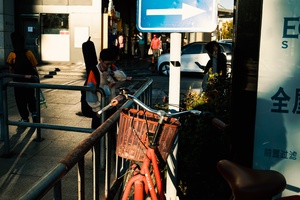 人行道上有一根金属杆上挂着一块蓝色标志 人行道上停着一辆橙色自行车 人行道上有人走动。
