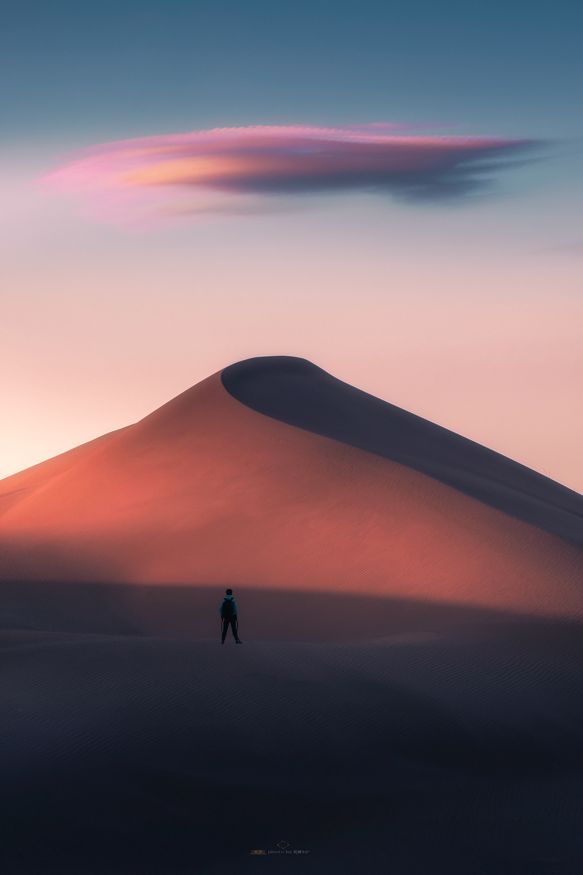 沙漠中的沙丘顶部站立着一个人 天空中飘着云彩 夕阳西下。