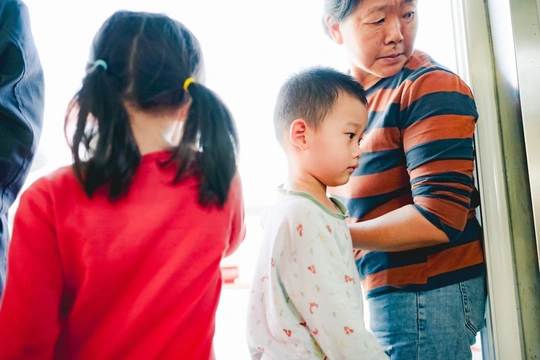 一个年轻男孩和一个小女孩正在窗户边看着 后面有成年人。