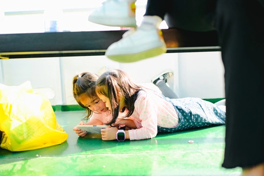 一个小女孩躺在地板上看手机 另一个年轻的孩子躺在她前面