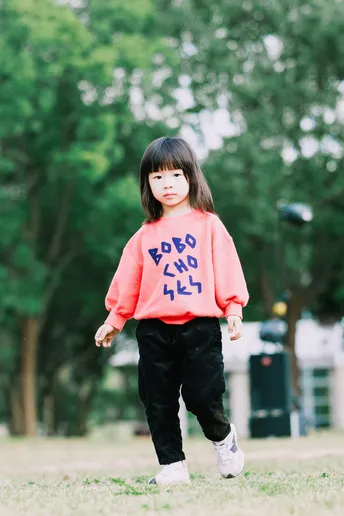 一个小女孩穿着一件印有“kids”字样的运动衫站在公园的草地上
