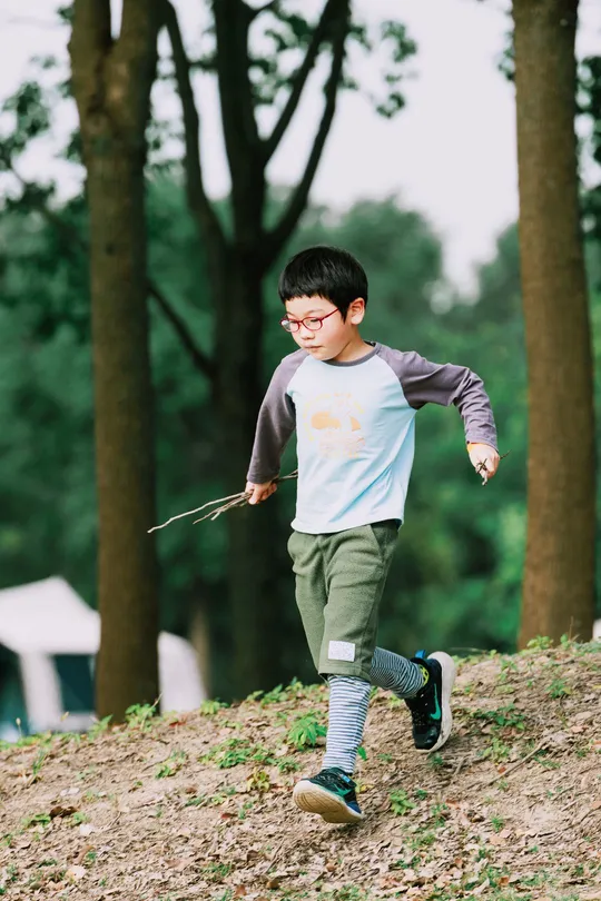 一个男孩在森林里跑下一个小山坡 手里拿着一个木棍和一只风筝。