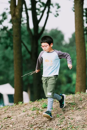 一个男孩在森林里跑下一个小山坡 手里拿着一个木棍和一只风筝。