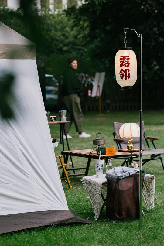 公园里一个站在白色帐篷旁边的人 旁边有一个桌子和椅子。