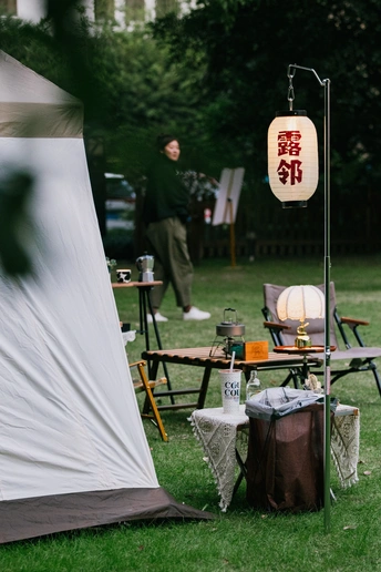 公园里一个站在白色帐篷旁边的人 旁边有一个桌子和椅子。