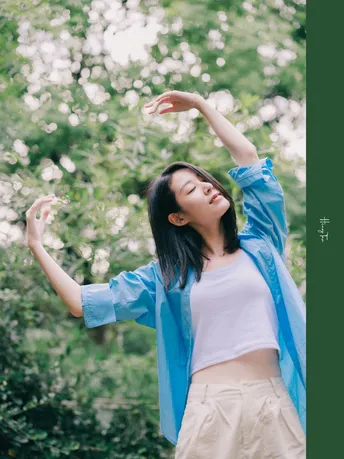 一位穿着蓝色衬衫的年轻女子站在森林中 双手举向天空。