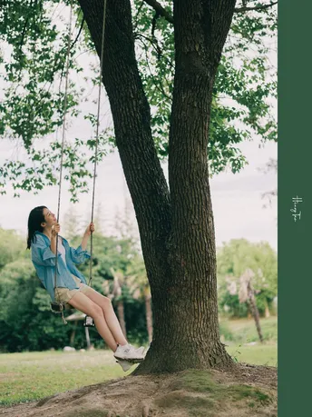 一位年轻女子坐在树下的秋千上