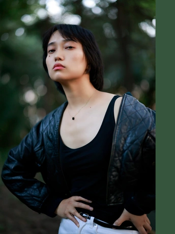 一个穿着黑色皮夹克站在树木丛中的年轻女子