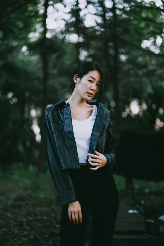 一个穿着黑色夹克和白色裤子的年轻女子站在森林中