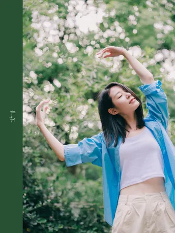 一位穿着蓝色衬衫的年轻女子站在森林中 双臂伸向天空。