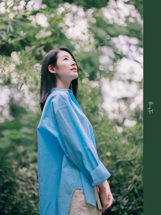 一位穿着蓝色衬衫的女士站在森林中 周围有树木。