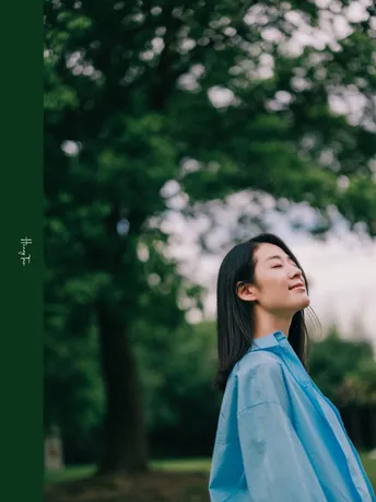 一位穿着蓝色衬衫的年轻女子在公园下撑着一把伞。
