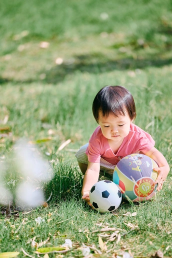 一个小女孩坐在草地上玩球 一个年轻男孩在田地里玩耍。