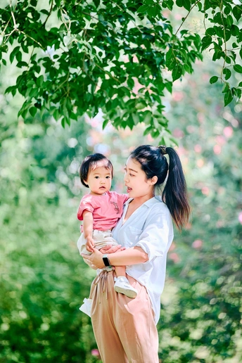 一位年轻女子抱着一个小女孩站在公园里一棵树下