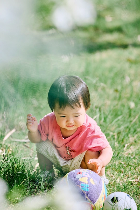 一个小女孩坐在草地上 在田野里玩着一个小球。