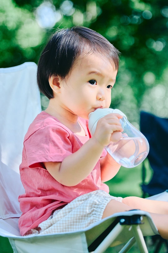 一个小女孩坐在草椅上喝着一瓶水或牛奶 旁边还有一个坐在草椅上的小男孩。