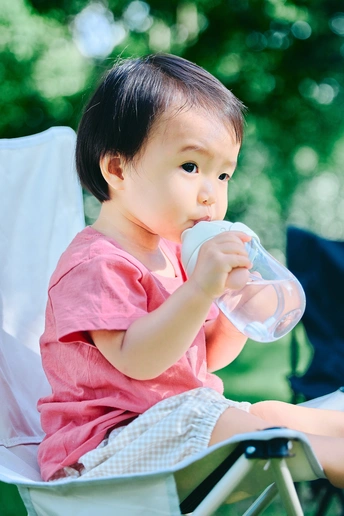 一个小女孩坐在草椅上喝着一瓶水或牛奶 旁边还有一个坐在草椅上的小男孩。