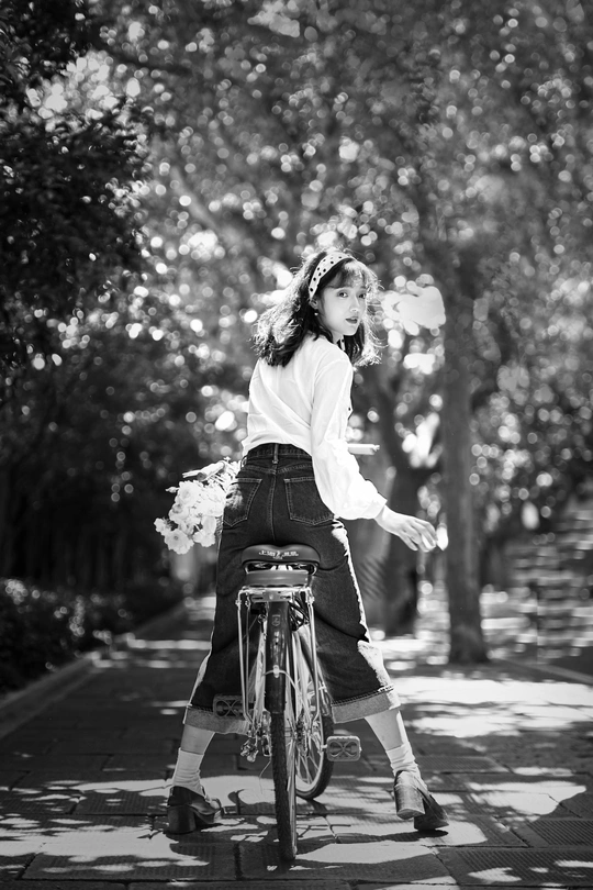 一张黑白照片 一位年轻女子骑自行车沿着街道行驶。