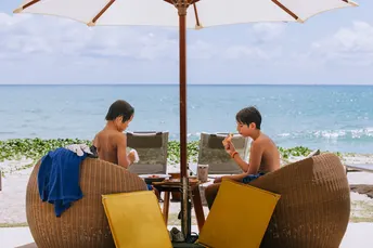 一个男子和一个年轻男孩坐在桌子旁的一张椅子上 靠近海洋 旁边有一台笔记本电脑。