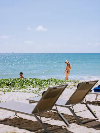 空荡荡的海滩 有椅子和遮阳伞 一位女士站在水中 眺望着海洋。