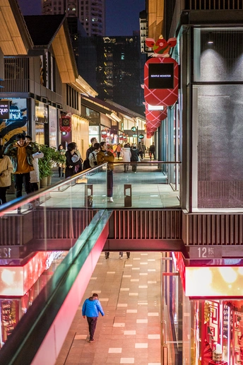 夜晚的一个购物中心 人们沿着街道走 一个女子沿着扶梯走