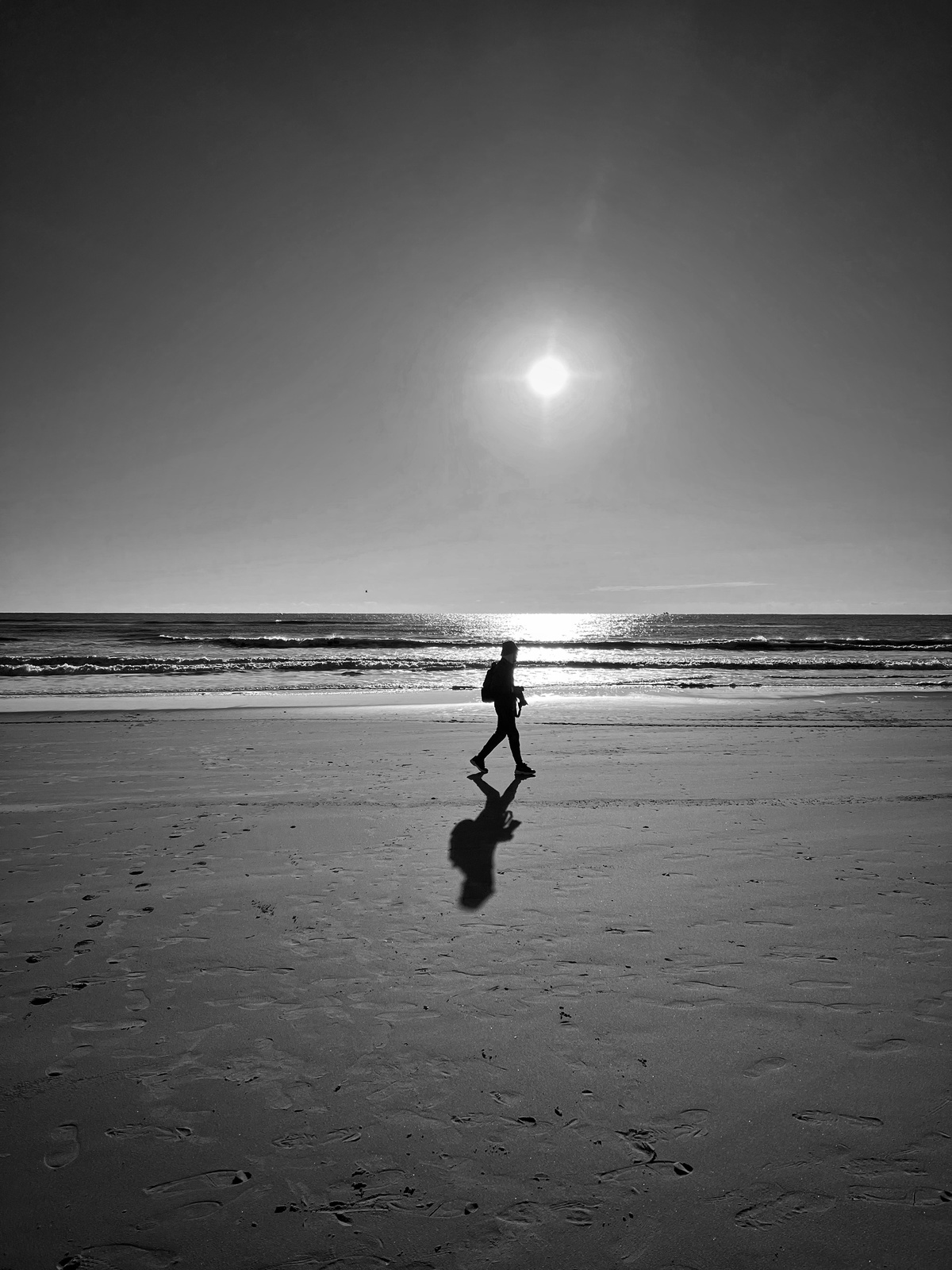 一个人在沙滩上行走 手里拿着一个球 背景是太阳
