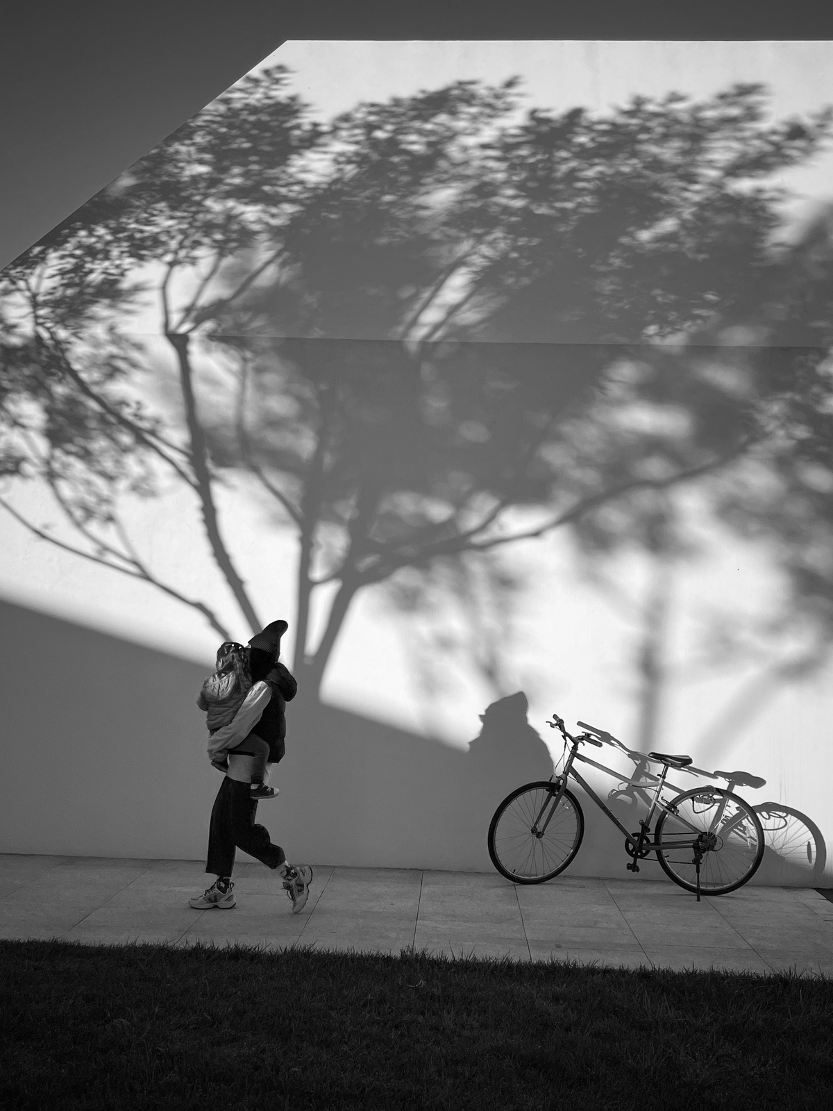 一张黑白照片 一个人背着书包走在人行道上 墙上有树的阴影。