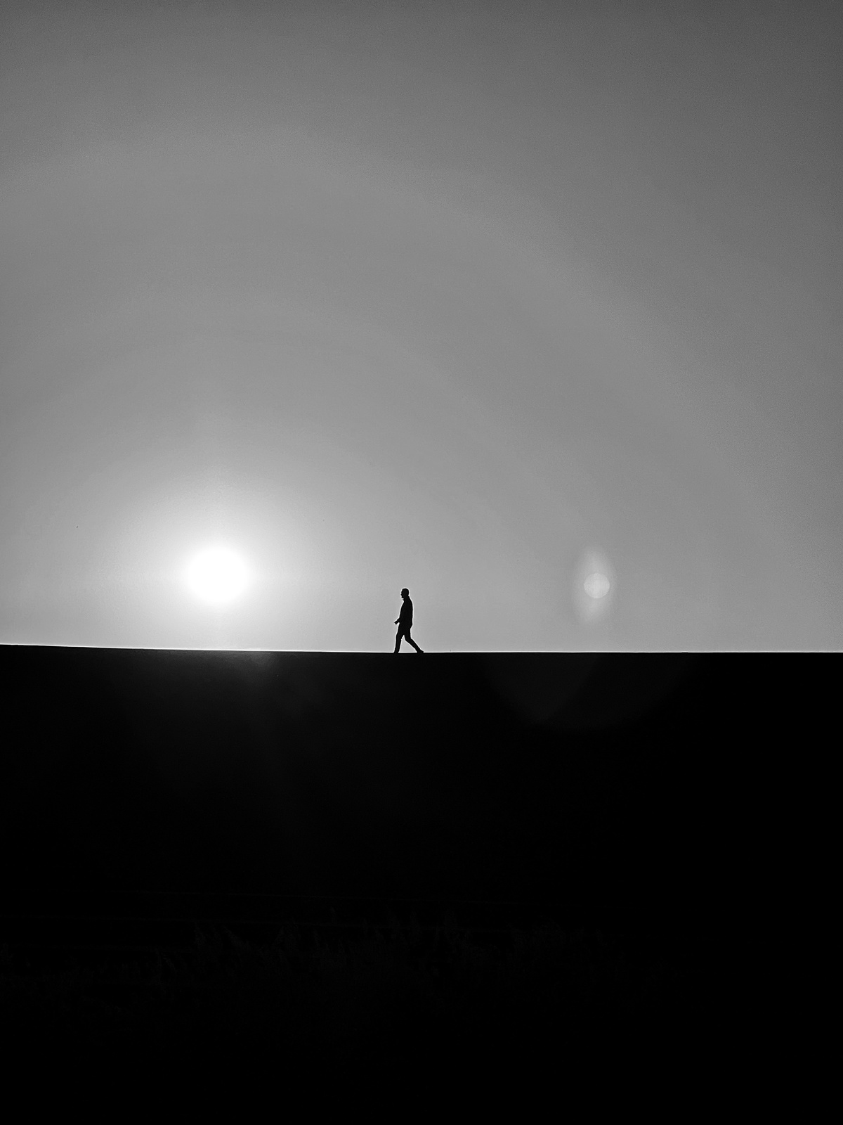 一个黑白剪影 一个人在山顶上行走 太阳低垂在天空中。