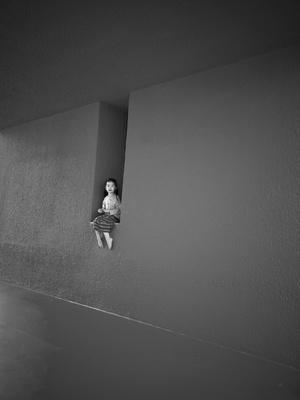 一个小女孩坐在墙边 透过一个小窗户向外看。