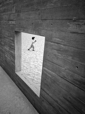 一张黑白照片 一个人在沙滩上行走 一个男孩在木质建筑物的窗户里奔跑。