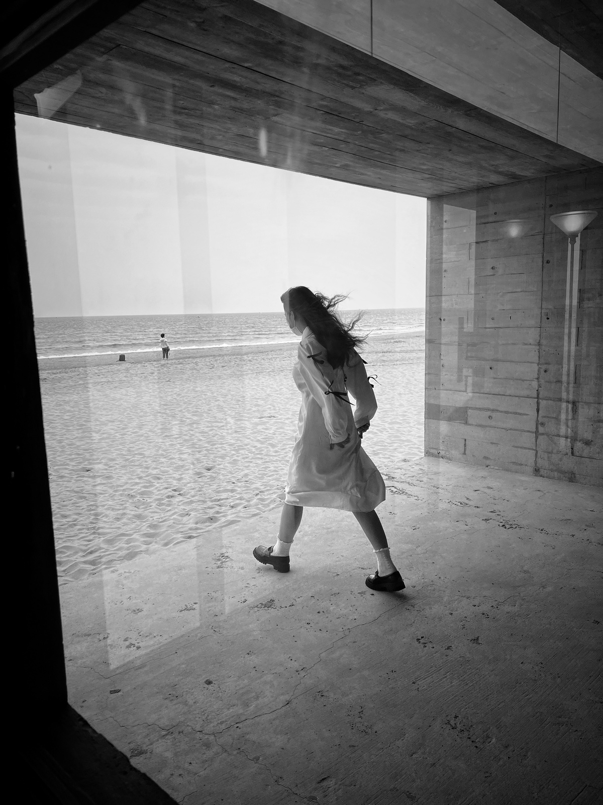 一位穿着黑白裙子的年轻女子在靠近水边的海滩上行走。