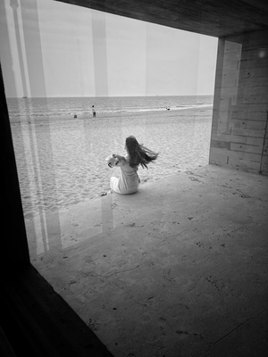 一位年轻女子坐在海滩上 带着她的小狗 凝视着窗外的水面。