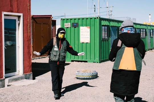 一些穿黑色衣服的人站在一个绿色容器和一些建筑物外面。