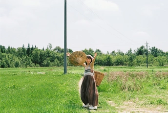 一个穿着连衣裙的女人撑着伞站在草地上