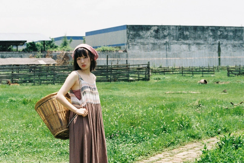 一个穿着连衣裙的年轻女子提着篮子穿过草地