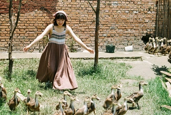 一个穿着连衣裙的年轻女子站在院子里的几只鸭子面前