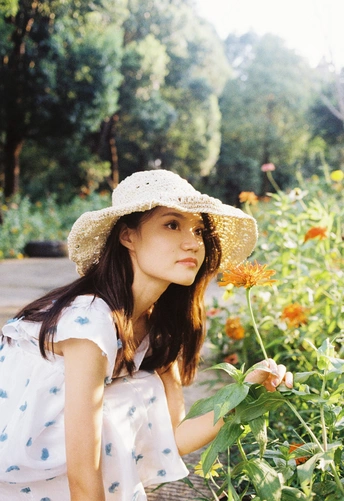 一位戴着帽子、穿着连衣裙的年轻女子站在花丛中