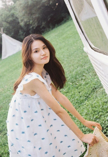 一位身穿蓝白相间连衣裙的年轻女子撑着一把白色雨伞站在一个白色帐篷前