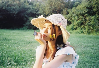 一个穿着白色连衣裙、戴着草帽的年轻女子坐在田里吃花