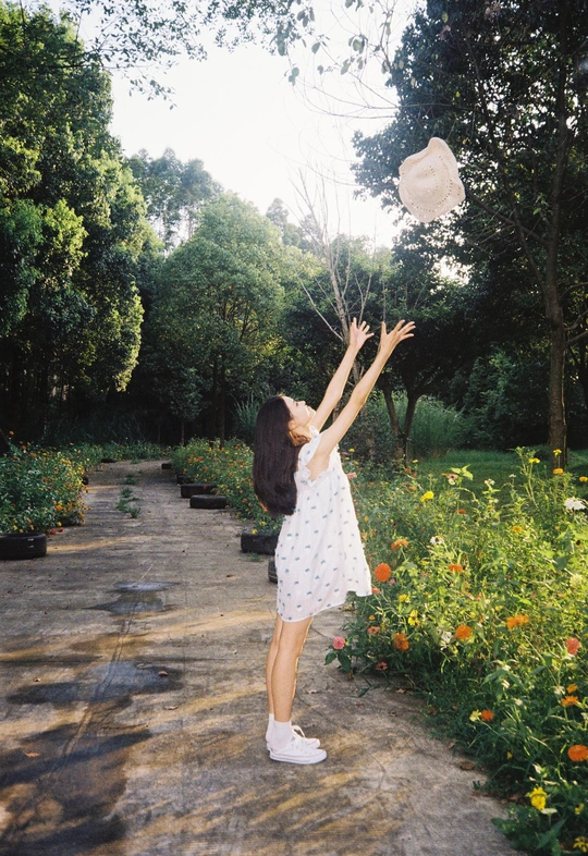 一位身穿白色连衣裙的年轻女子撑着雨伞 向花园里扔气球