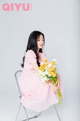 一个穿着粉红色连衣裙的年轻女子抱着一束花坐在椅子上