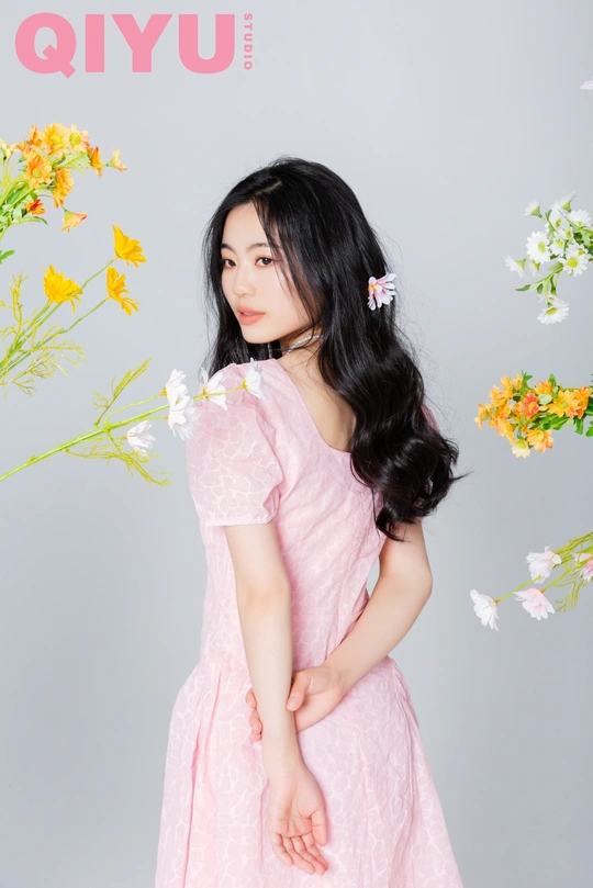 一位长发年轻女子穿着粉色裙子站在杂志封面有花的面前