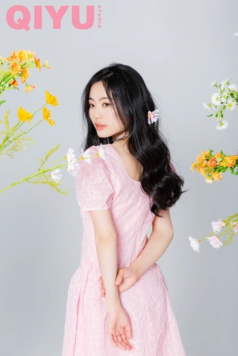 一位长发年轻女子穿着粉色裙子站在杂志封面有花的面前