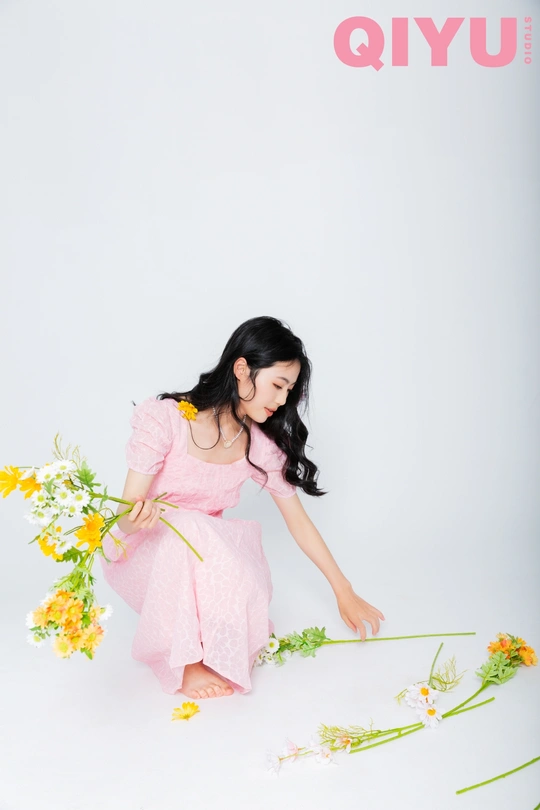 一位穿着粉红色连衣裙的年轻女子正在与花拍照