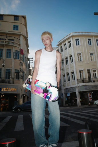 一个穿着白色牛仔裤的年轻人 holding a skateboard standing in the